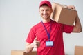 Delivery guy isolated on white wall standing carrying box on shoulder showing thu,b up positive Royalty Free Stock Photo