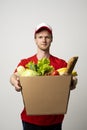 Delivery male employee in a red uniform holds paper cardbox package with groceries. Products delivery from shop or restaurant to
