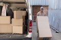 Delivery man carrying cardboard boxes on trolley near van outside the warehouse Royalty Free Stock Photo