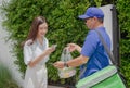 Delivery man delivering food to a beautiful Asian girl in front of the house. payments contactless with smartphone, scanning QR