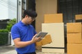 Delivery man holding a cardboard box and checking or input information on digital tablet next to a vehicle loaded with Royalty Free Stock Photo
