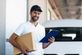 Delivery man is holding a cardboard box and a clipboard and posing Royalty Free Stock Photo