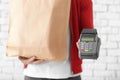 Delivery man holding paper bag with food and payment terminal on brick wall background Royalty Free Stock Photo