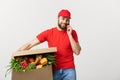 Delivery man holding paper box with food and making a call with mobile phone isolated over grey background. Royalty Free Stock Photo