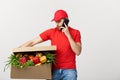 Delivery man holding paper box with food and making a call with mobile phone isolated over grey background. Royalty Free Stock Photo