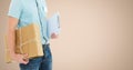 Delivery man holding parcel box and clipboard against beige background Royalty Free Stock Photo