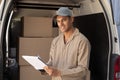 Delivery man looking at camera while writing on clipboard near van outside the warehouse Royalty Free Stock Photo