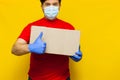 Delivery man in medical mask holding a cardbox on Yellow background Royalty Free Stock Photo