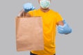 Delivery Man With Paper Bag in Hands Wearing Medical Mask and Gloves Showing Thumb Up Isolated Close Up. Yellow Uniform Indian