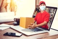 Delivery man in red shirt with hygienic mask, holding goods order in package parcel out from laptop computer with warehouse Royalty Free Stock Photo