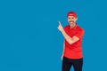 Delivery man in red uniform, cap and shirt, isolated on blue studio background. Professional male employee. Service concept