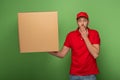 Delivery man in red uniform holding huge parcel and covering mouth on green