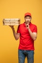 Delivery man in red uniform holding pizza boxes and showing shh sign isolated on yellow