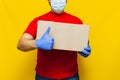 Delivery man in medical mask holding a cardbox on Yellow background Royalty Free Stock Photo