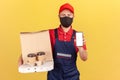 Delivery man in uniform and hygienic protective mask holding empty screen smartphone and coffee with pizza, online order fast and