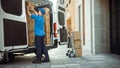 Delivery Man Uses Hand Truck Trolley Full of Cardboard Boxes and Packages, Loads Parcels into Truc Royalty Free Stock Photo