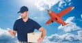 Delivery man using mobile phone while holding parcel against airplane flying in sky Royalty Free Stock Photo