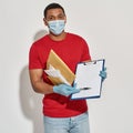 Delivery man wearing face mask and protective gloves holding parcels and envelopes, showing form for signing on Royalty Free Stock Photo