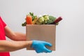 Delivery man wearing mask and gloves holding craft paper box full of different groceries.