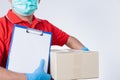 Delivery man wearing medical mask and gloves holding box package with paper on clipboard Isolated on a white studio background. Royalty Free Stock Photo