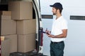 Delivery man writing on clipboard while standing next to his van Royalty Free Stock Photo