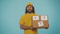 Delivery man in yellow uniform looking at the camera, holding a box with fragile stickers. Isolated on blue background. Royalty Free Stock Photo