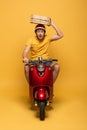 Delivery man in yellow uniform riding scooter with pizza boxes on yellow background