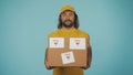 Delivery man in yellow uniform smiling, holding a box with fragile stickers. Isolated on blue background. Royalty Free Stock Photo