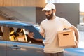 Arab Deliveryman Holding Parcel Looking At Clipboard Near Car Outdoors