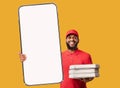 Delivery service app. African american courier man with pizza boxes holding huge smartphone with white screen, mockup Royalty Free Stock Photo