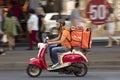 Delivery service courier riding a red and beige vintage vespa scooter in the city street traffic