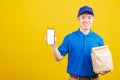 Delivery service man smiling wearing blue uniform hold paper containers for takeaway bag grocery food packet and show smartphone Royalty Free Stock Photo
