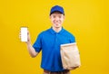 Delivery service man smiling wearing blue uniform hold paper containers for takeaway bag grocery food packet and show smartphone Royalty Free Stock Photo