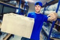 A delivery service worker holds a box in his hands against the background of the warehouse racks.