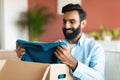 Glad contented Indian buyer man unpacking box with clothes indoor Royalty Free Stock Photo