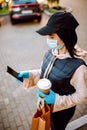 Delivery woman in protective face mask and gloves with a bag of food and coffee checking addres with her smartphone. Health Royalty Free Stock Photo