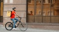 Delivery, work and sport. Young guy with beard in helmet with backpack rides a bicycle down the street