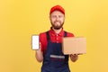 Deliveryman holding cardboard box with ordered online goods, showing cell phone with empty screen. Royalty Free Stock Photo