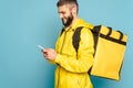 Deliveryman in yellow uniform with backpack using smartphone on blue background