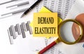 DEMAND ELASTICITY text on a sticky on the graph background with pen and magnifier Royalty Free Stock Photo