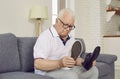 Demented retired senior man sitting on couch and choosing which type of shoes to wear