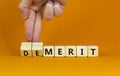 Demerit or merit symbol. Businessman turns wooden cubes and changes words `demerit` to `merit`. Beautiful orange table, orange