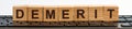 DEMERIT word made with building blocks. A row of wooden cubes with a word written in black font is located on a black keyboard