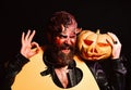 Demon with smile holds jack o lantern and shows ok sign. Halloween party concept. Man wearing scary makeup holds cut Royalty Free Stock Photo