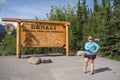 DENALI NATIONAL PARK ALASKA: A blonde tourist woman uses a selfie stick to take a photo for social media by the sign