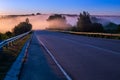 Dence early morning fog in wold at summer highway near river with guard rails Royalty Free Stock Photo