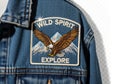 Denim jacket with embroidered patch of an eagle soaring over mountains and the words wild spirit explore isolated on white Royalty Free Stock Photo