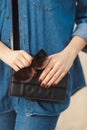 Denim outfit fashion details. Stylish woman with red glitter manicure in navy jeans holding sunglasses and leather small cross bod Royalty Free Stock Photo