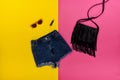 Denim shorts, black handbag, lipstick and glasses. Bright yellow and pink background. Fashionable concept