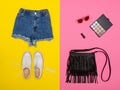 Denim shorts, white sneakers, black handbag, cosmetics. Bright yellow and pink background.